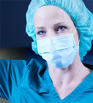 Chirurgin in blauer OP-Kleidung mit Maske und Haube, konzentriert während eines medizinischen Eingriffs
